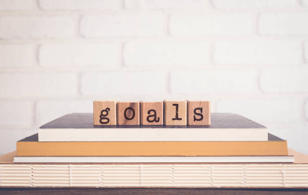 The word GOALS, alphabets on wooden rubber stamps on top of books with bricks background, blank copy space, vintage minimal style. Concepts of success, project planning and business management.